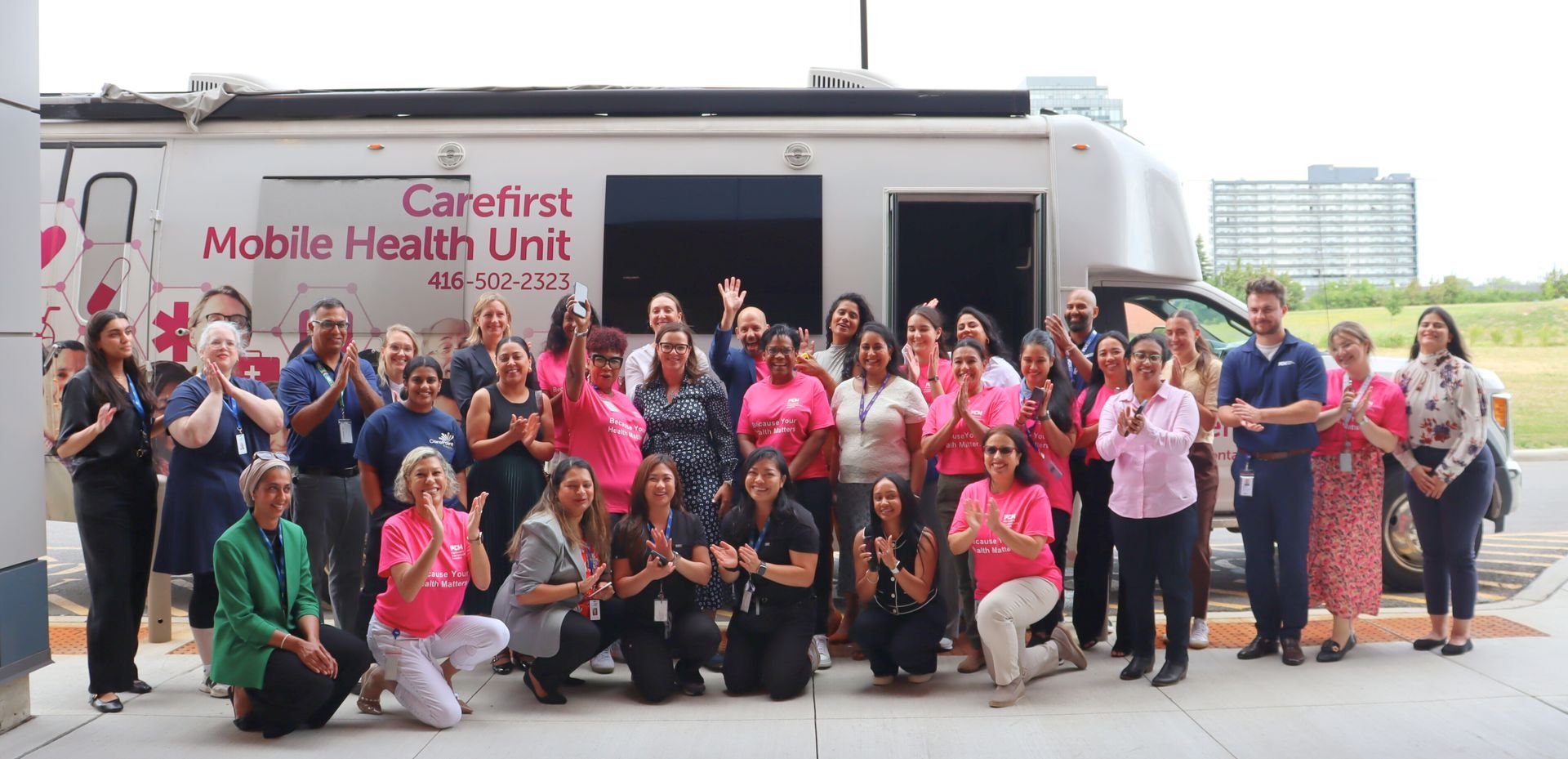 Group of people clapping in front of a Carefirst mobile health unit. Many wear pink.