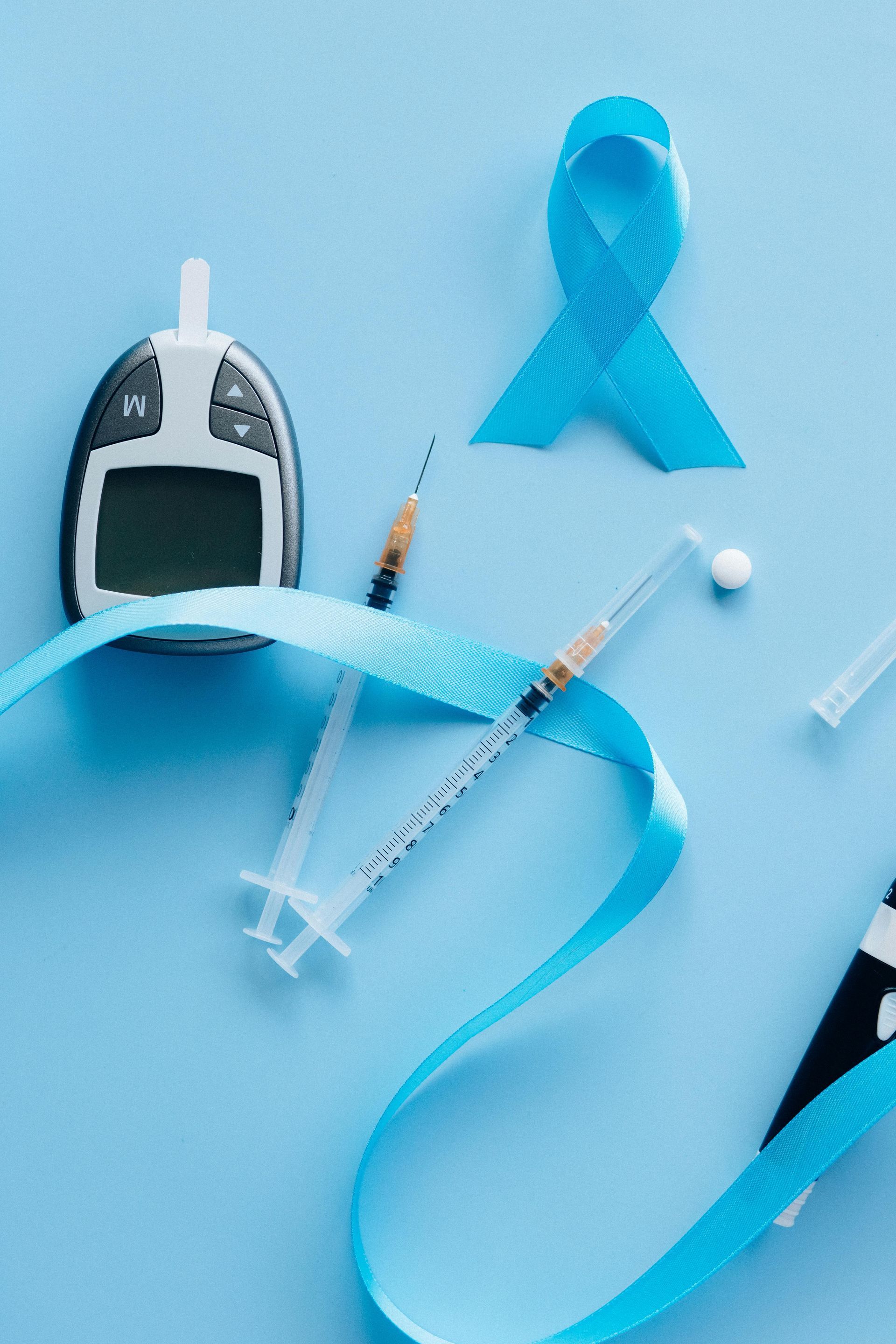 Diabetes awareness: Blue ribbon, glucometer, syringes, and pills on a light blue background.