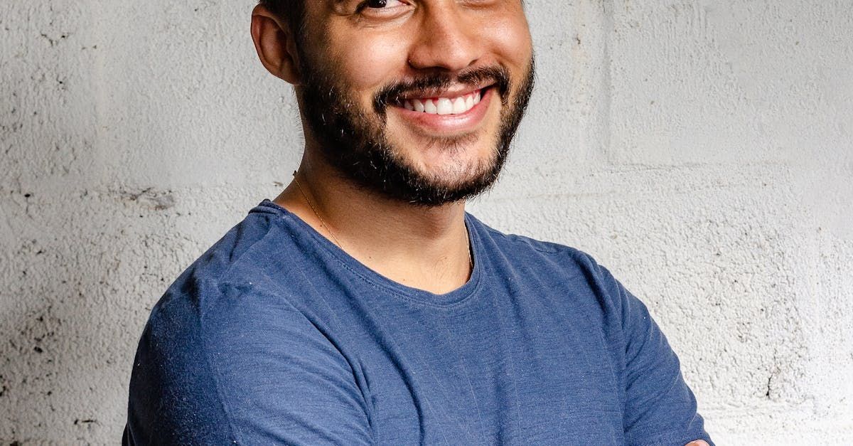 A man with a beard is smiling with his arms crossed and wearing a blue shirt.