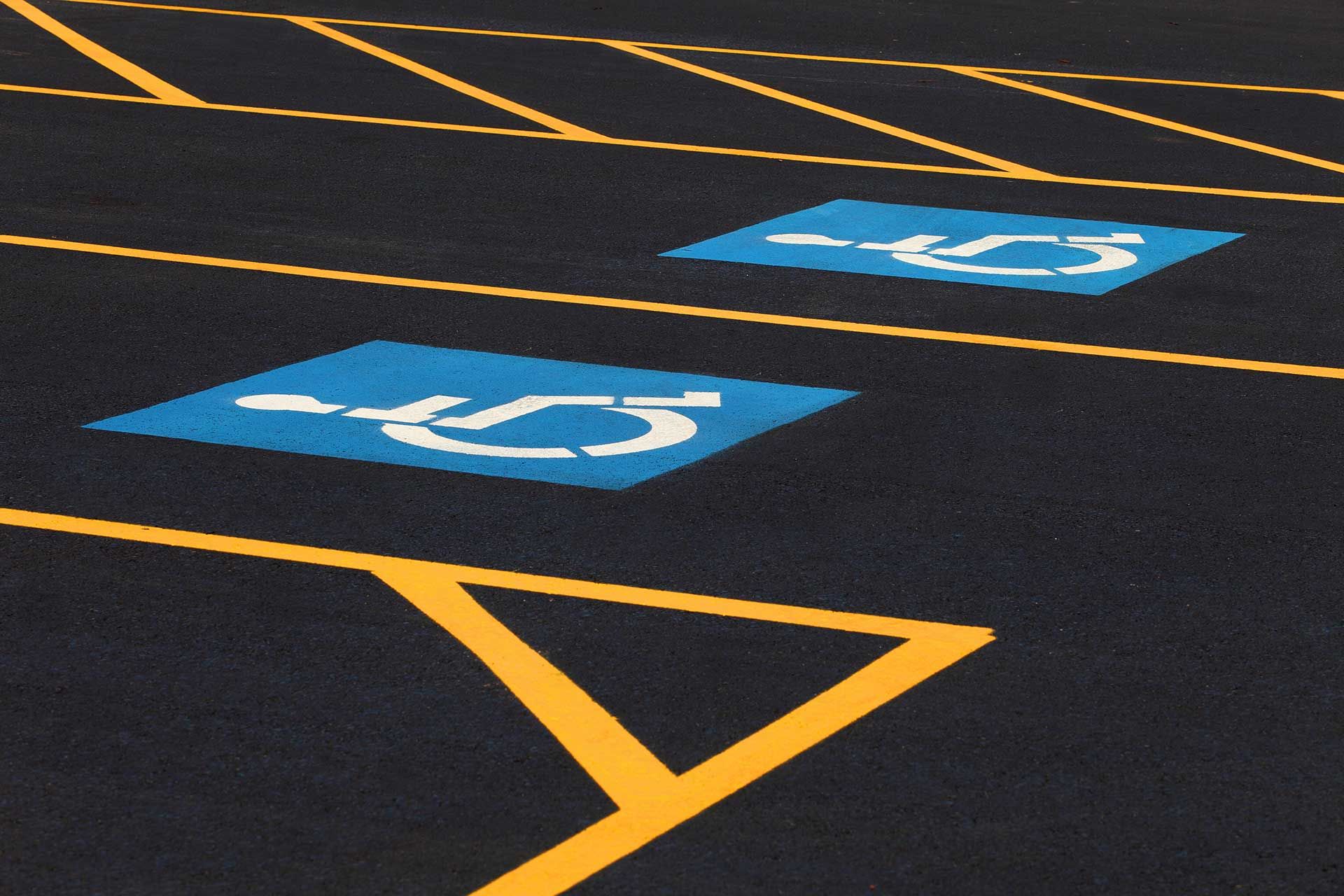 Two blue accessible parking symbols painted on black asphalt with yellow-lined safety access aisles.