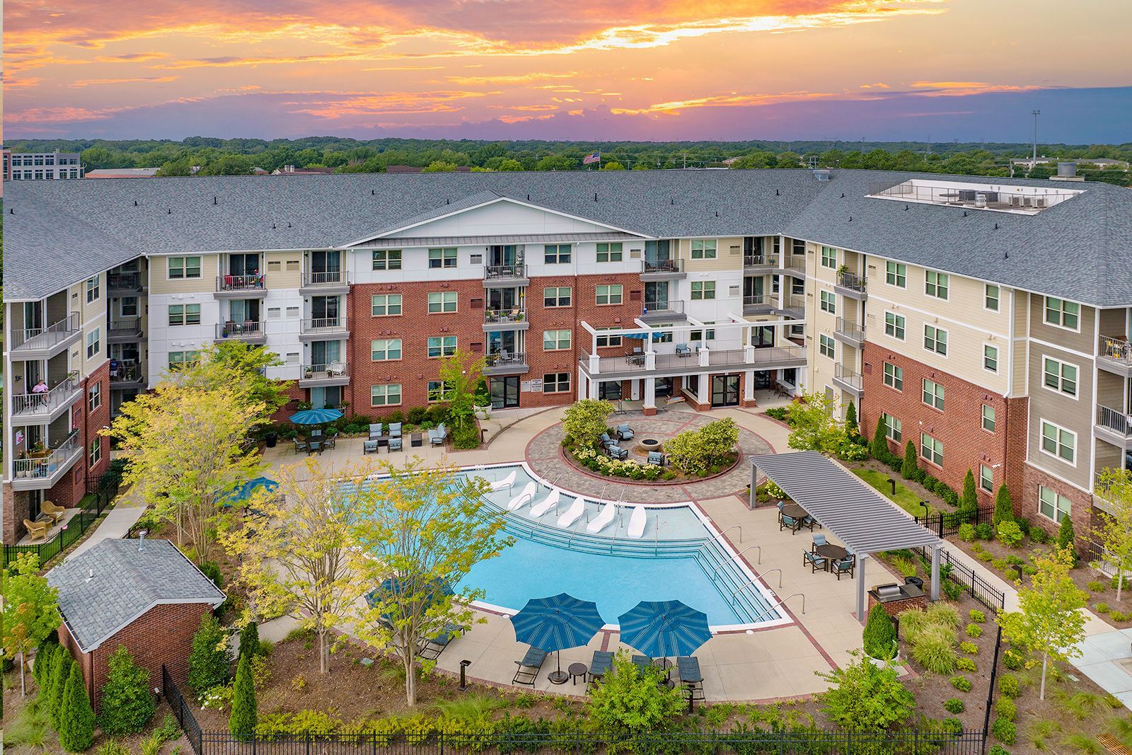 Apartment complex with pool. Buildings surround a pool, lush landscaping, and a sunset.