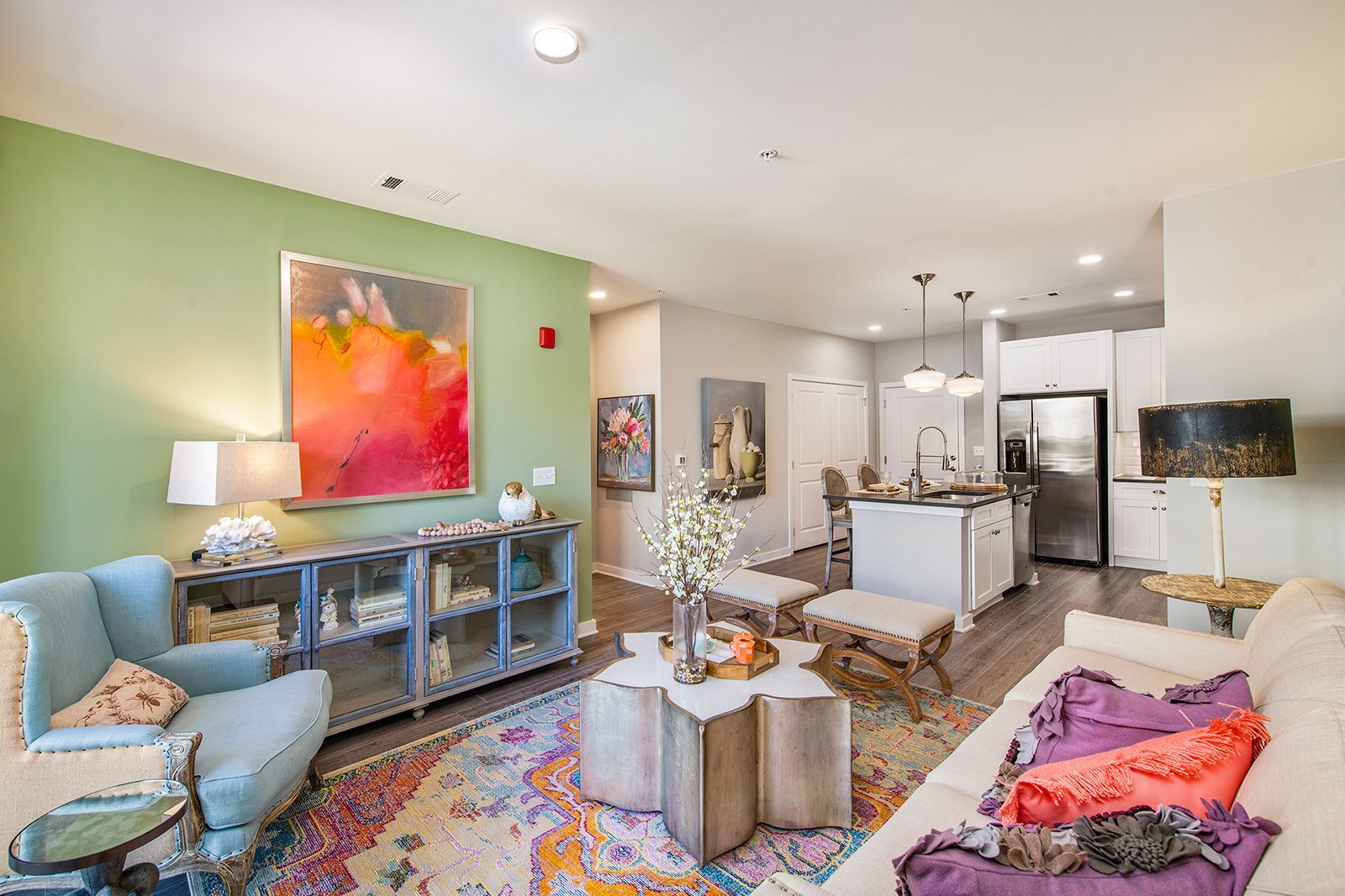 Living room with green wall, blue chair, floral rug, kitchen in the background.