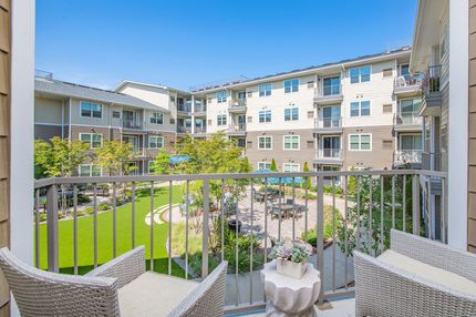 Balcony view of an apartment courtyard, two chairs, greenery, and multi-story buildings.