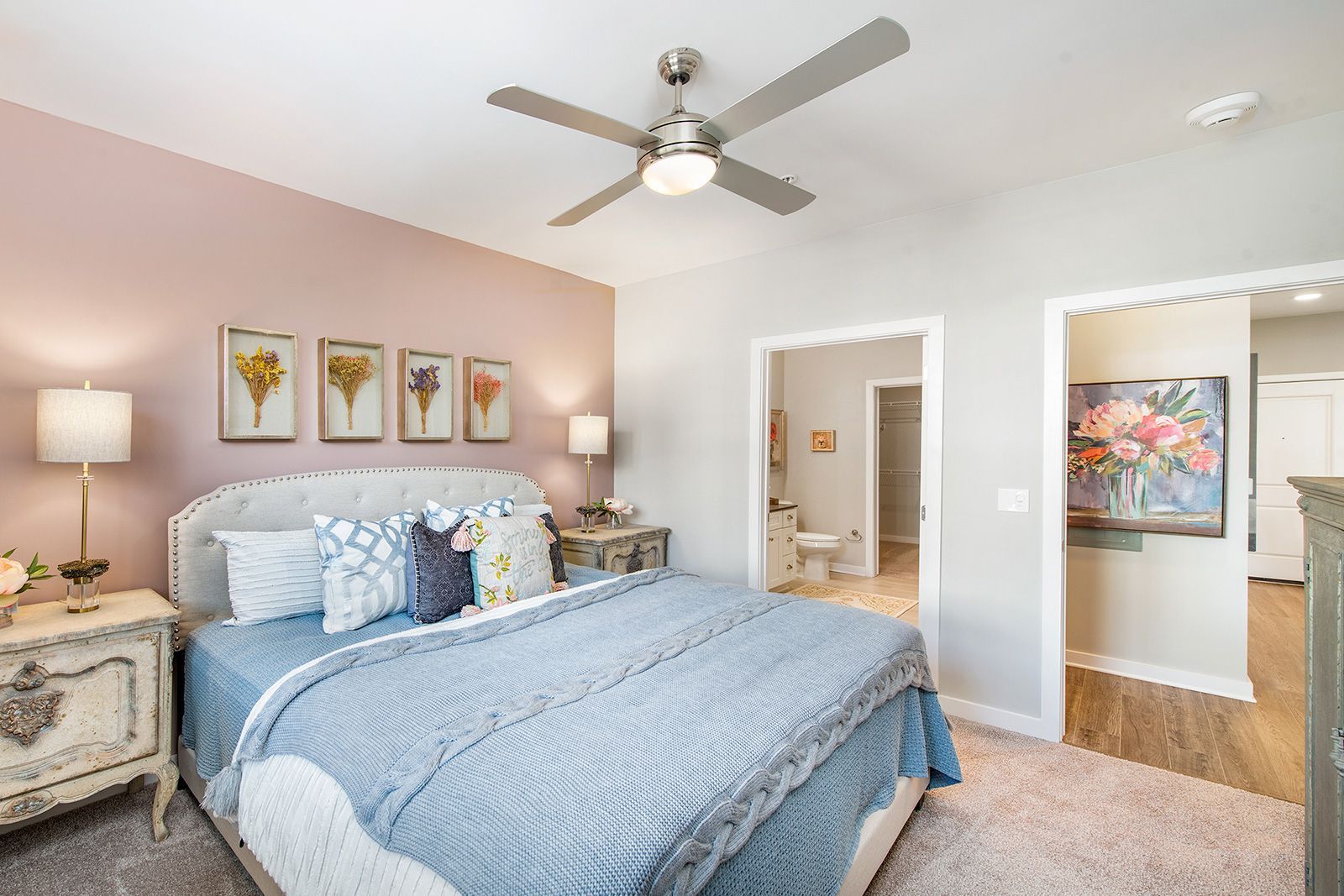 Bedroom with pink wall, gray curtains, bed with blue bedding, nightstands, and decor.