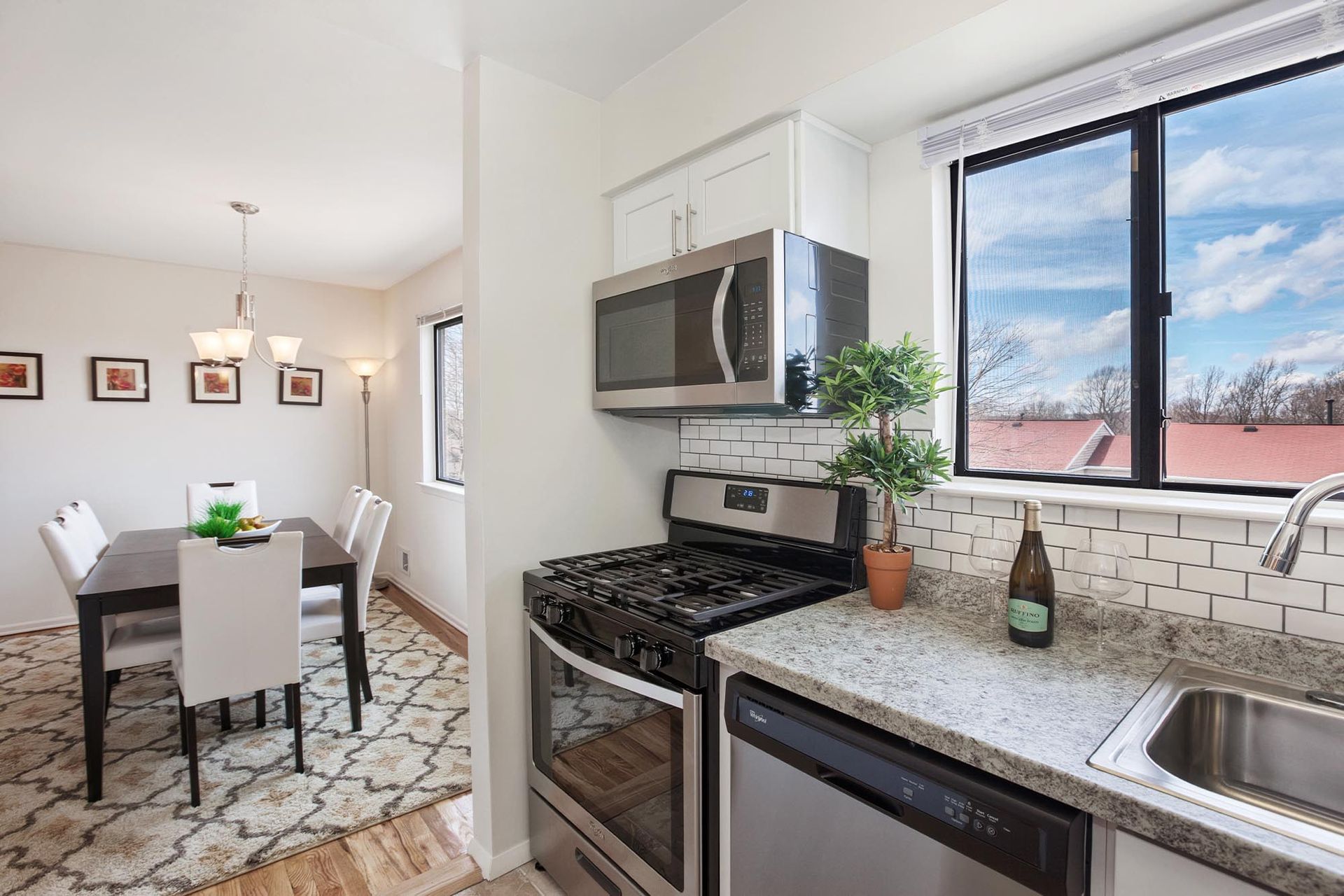 Modern kitchen with stainless steel appliances, granite counters, white cabinets, and a dining area.
