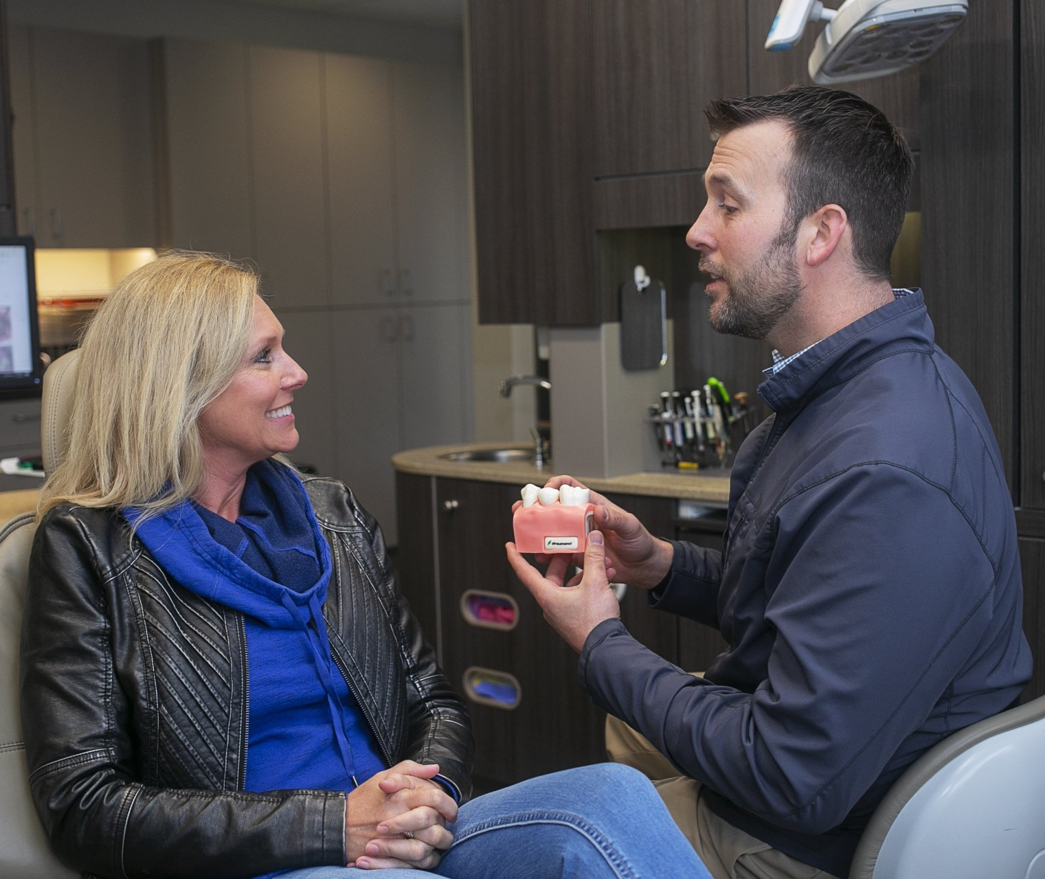 Visit the best dentist for dentures in Lawson, MO. A man is holding a model of a woman 's teeth while talking to her.