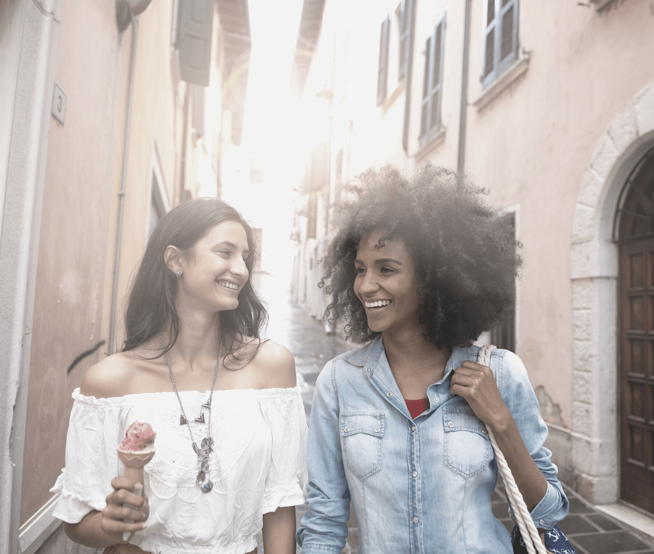 Two women are walking down a street and one is holding an ice cream cone.