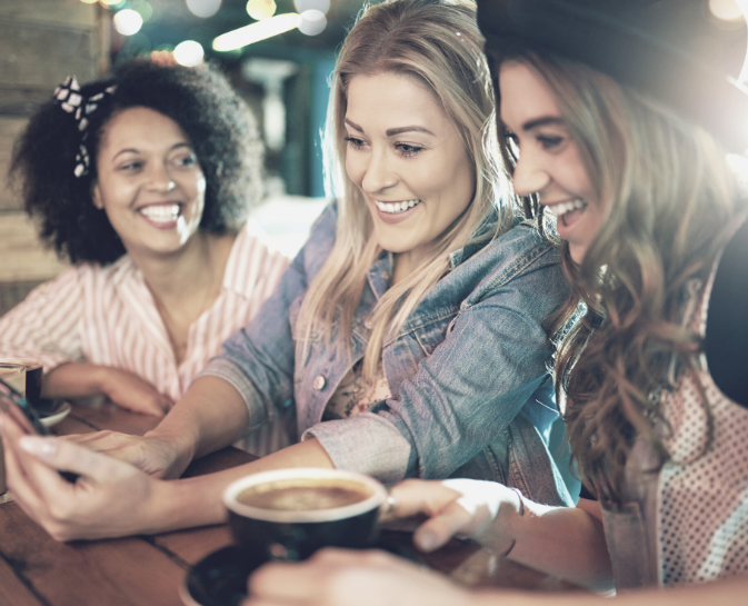 Three women are sitting at a table drinking coffee and looking at their phones.