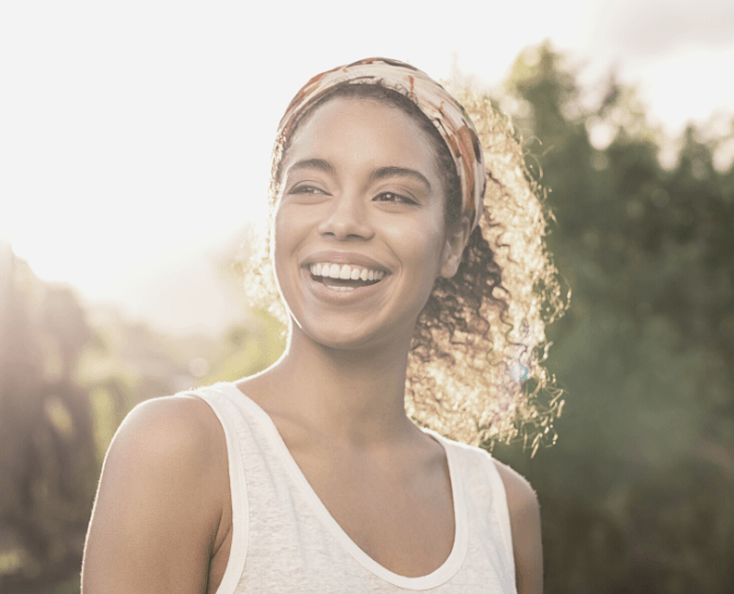 A woman wearing a headband and a white tank top is smiling.