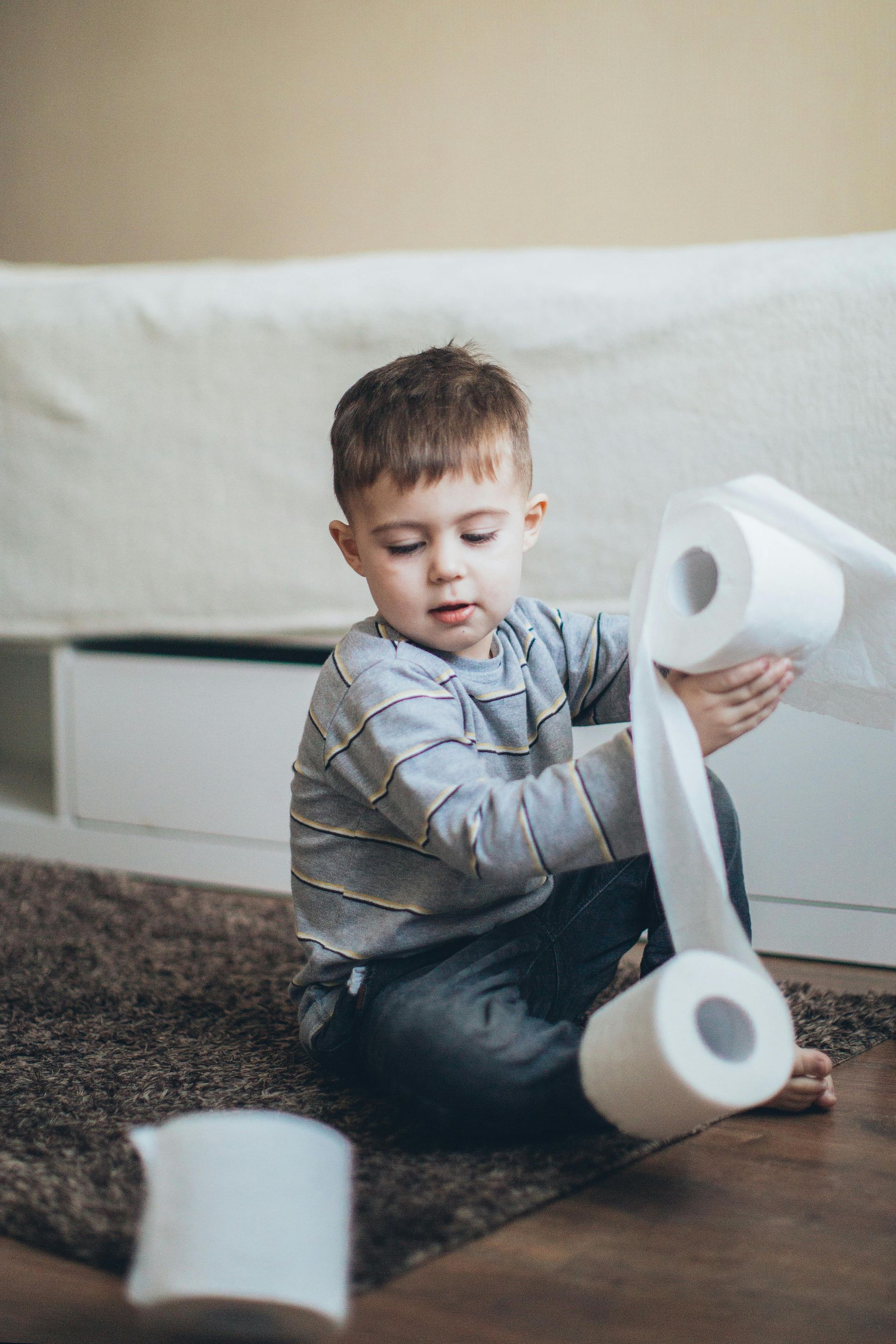 Young child playing with multiple rolls of toilet paper on a rug.