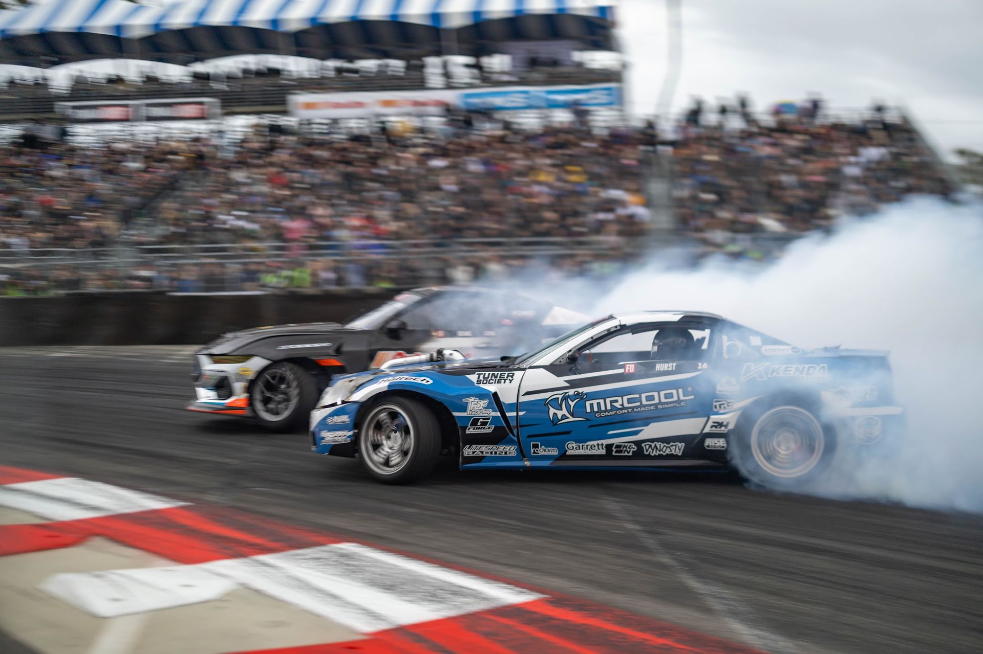 Two cars are racing on a race track with smoke coming out of their tires.