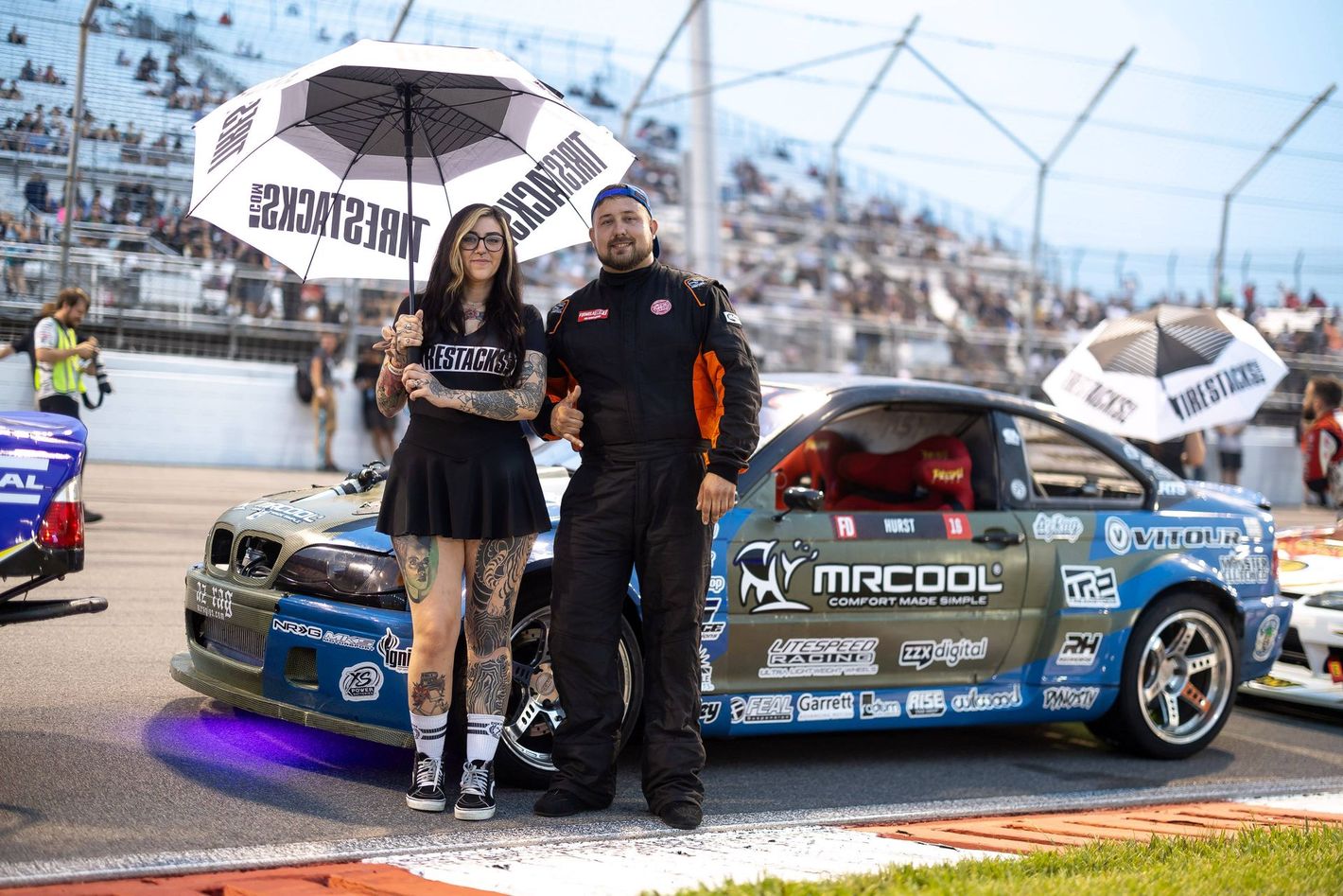A man and a woman are standing next to a race car on a track.