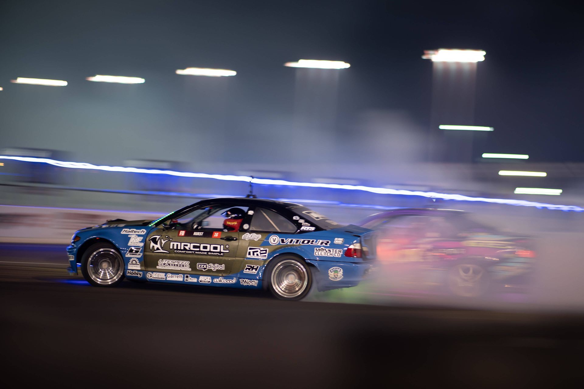 A blue car is drifting on a race track at night.
