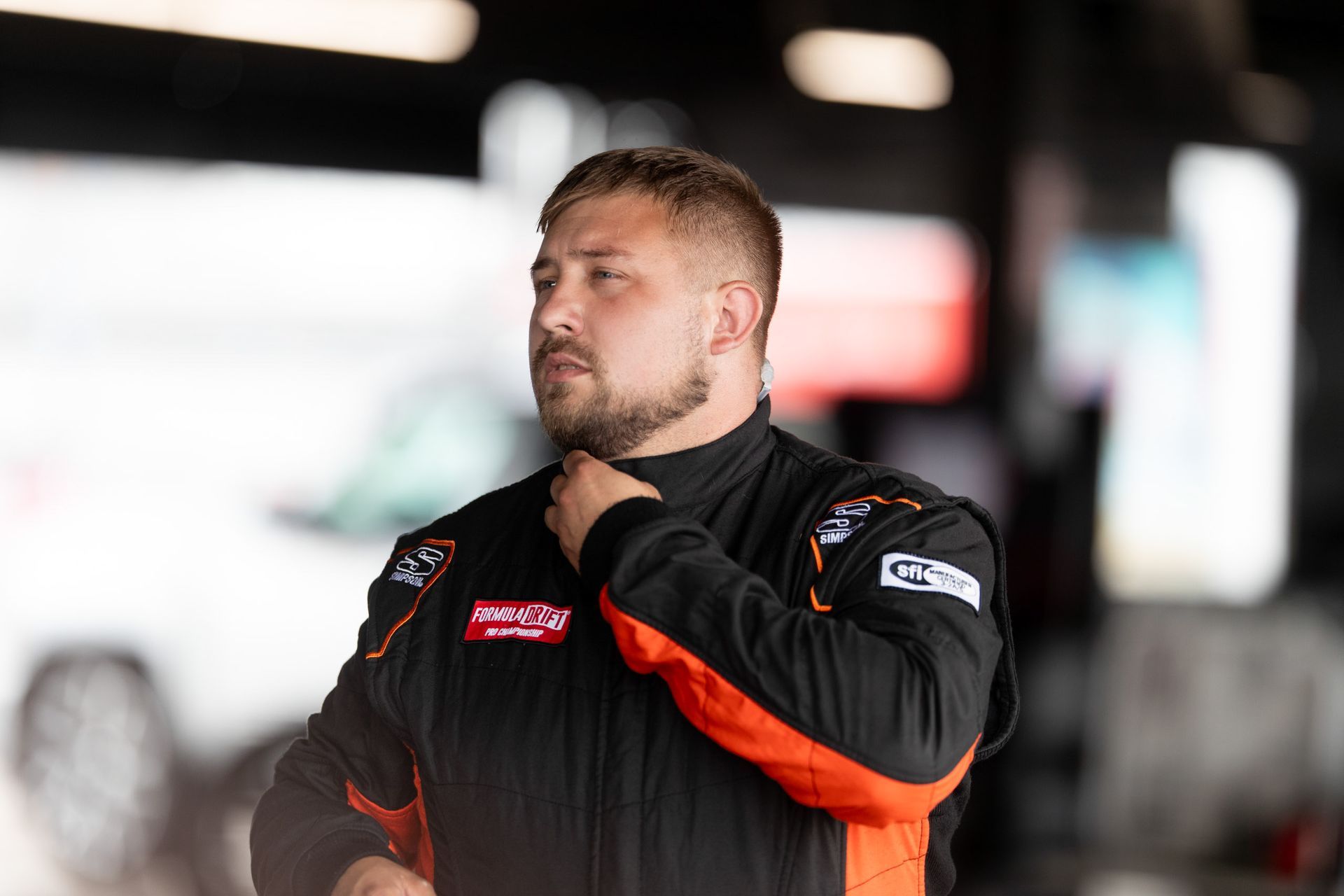 A man with a beard is wearing a black and orange racing suit.