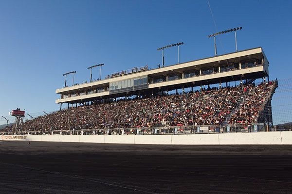 A large crowd of people are watching a race at a race track.