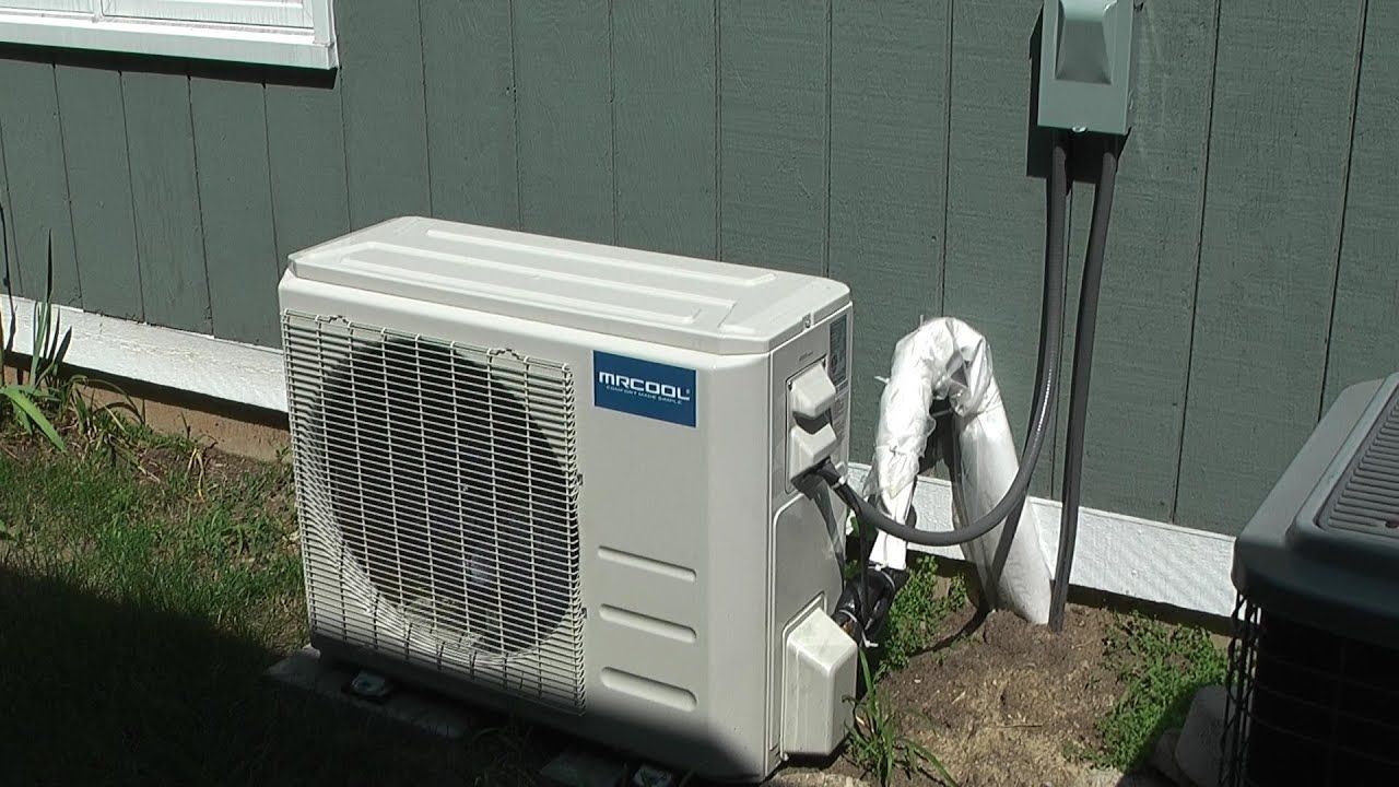 A white air conditioner is sitting outside of a house.