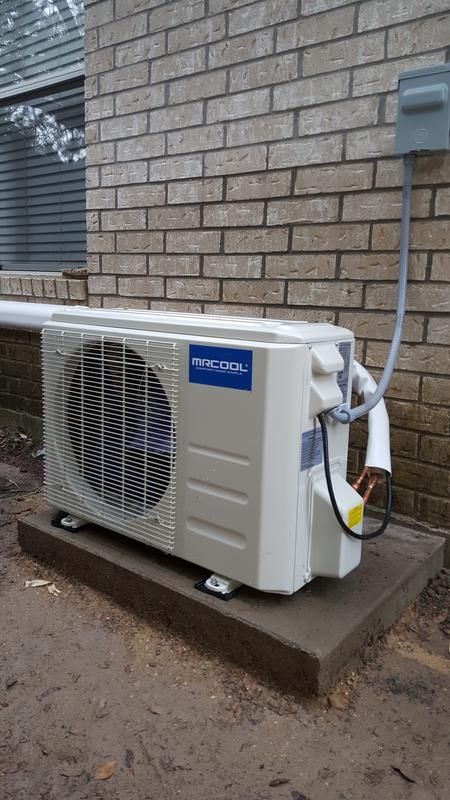 A white air conditioner is sitting outside of a brick building.