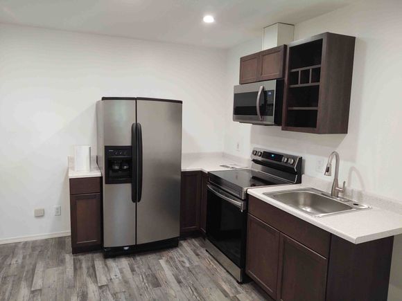 Modern kitchen with stainless steel appliances, dark wood cabinets, and white countertops