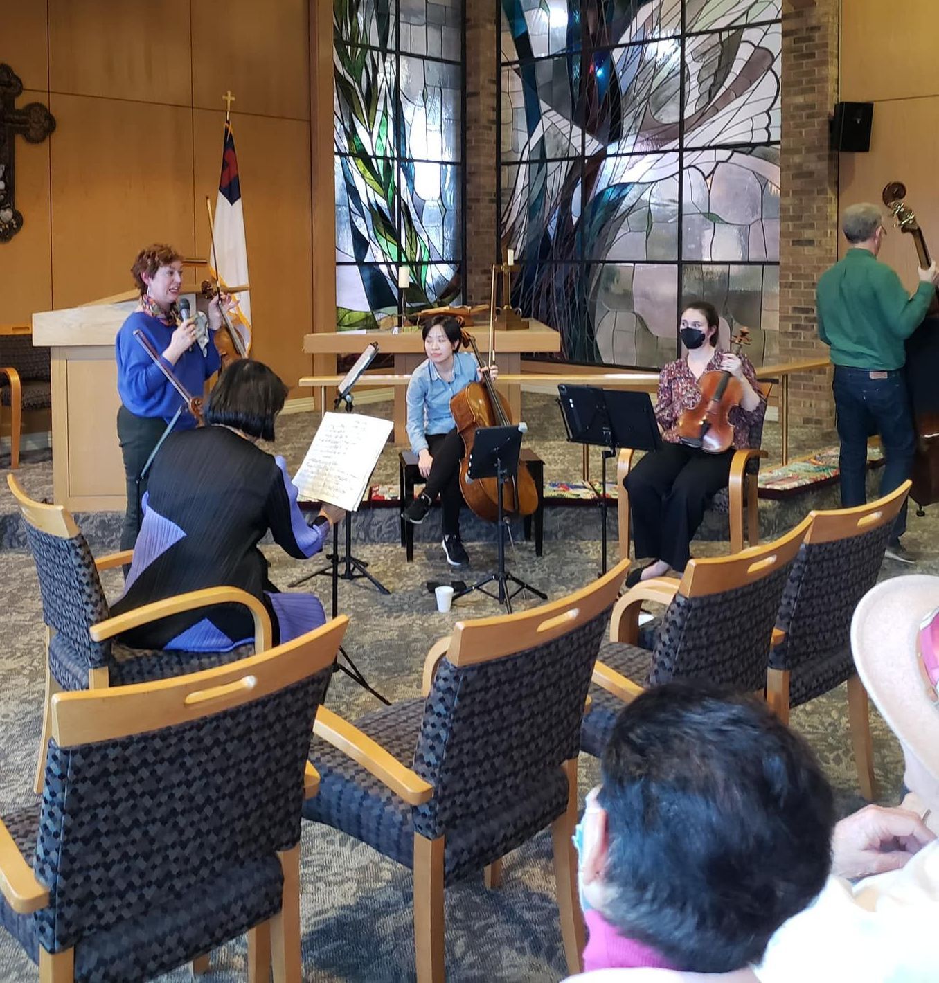 String ensemble performing in a church with stained glass. Musicians play in front of empty chairs.