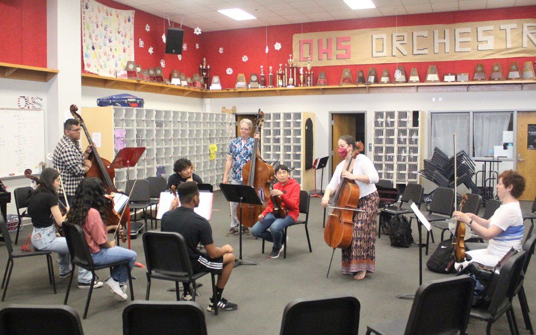 Orchestra rehearsal: Musicians playing stringed instruments in a room with trophies and 