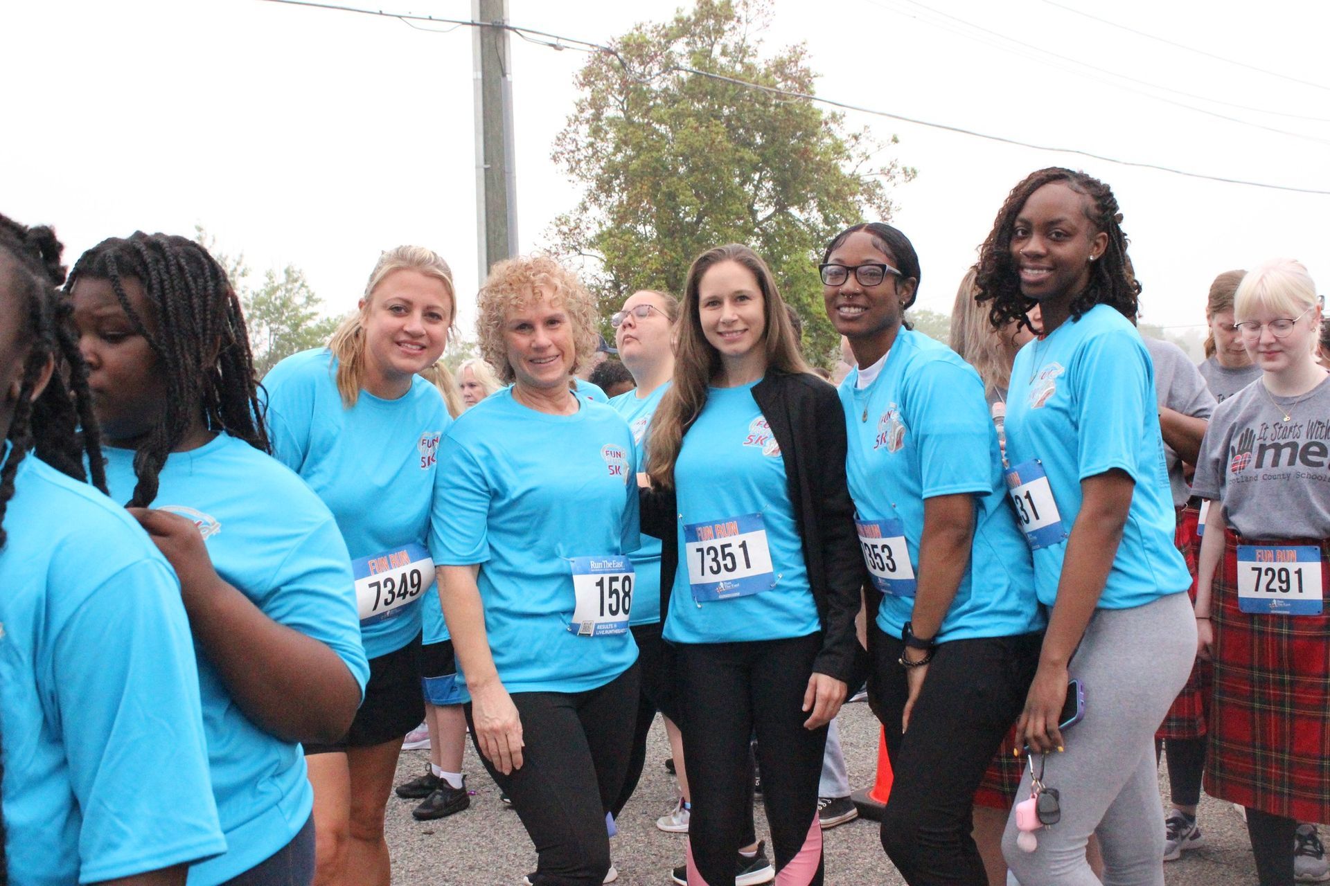 Group of people in matching blue shirts pose at an outdoor event. Some wear race bibs.