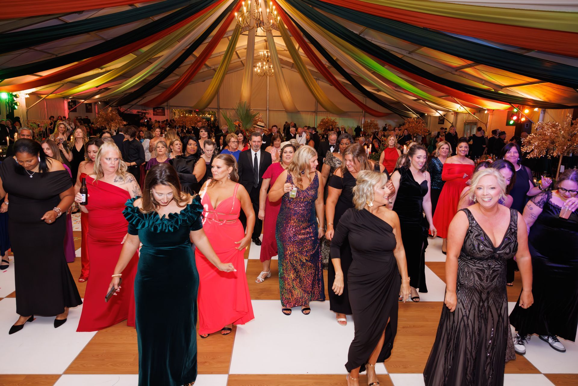 People dancing on a checkered floor under colorful draped ceiling in a tent.