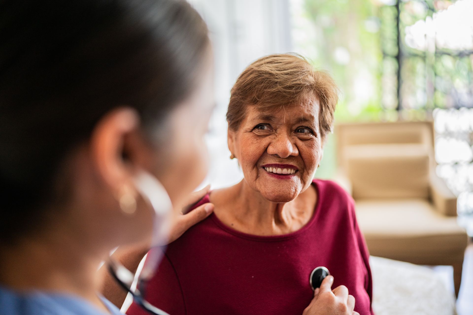 Doctor using stethoscope on smiling patient; indoor setting.