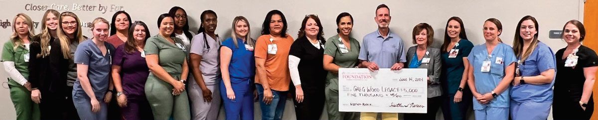 Group of people holding a large check. Some are in scrubs. Bright wall in the background.