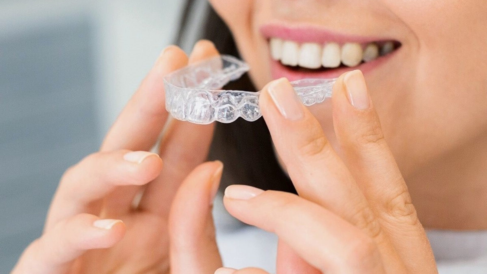 Person fitting a clear dental aligner over their teeth, smiling close-up