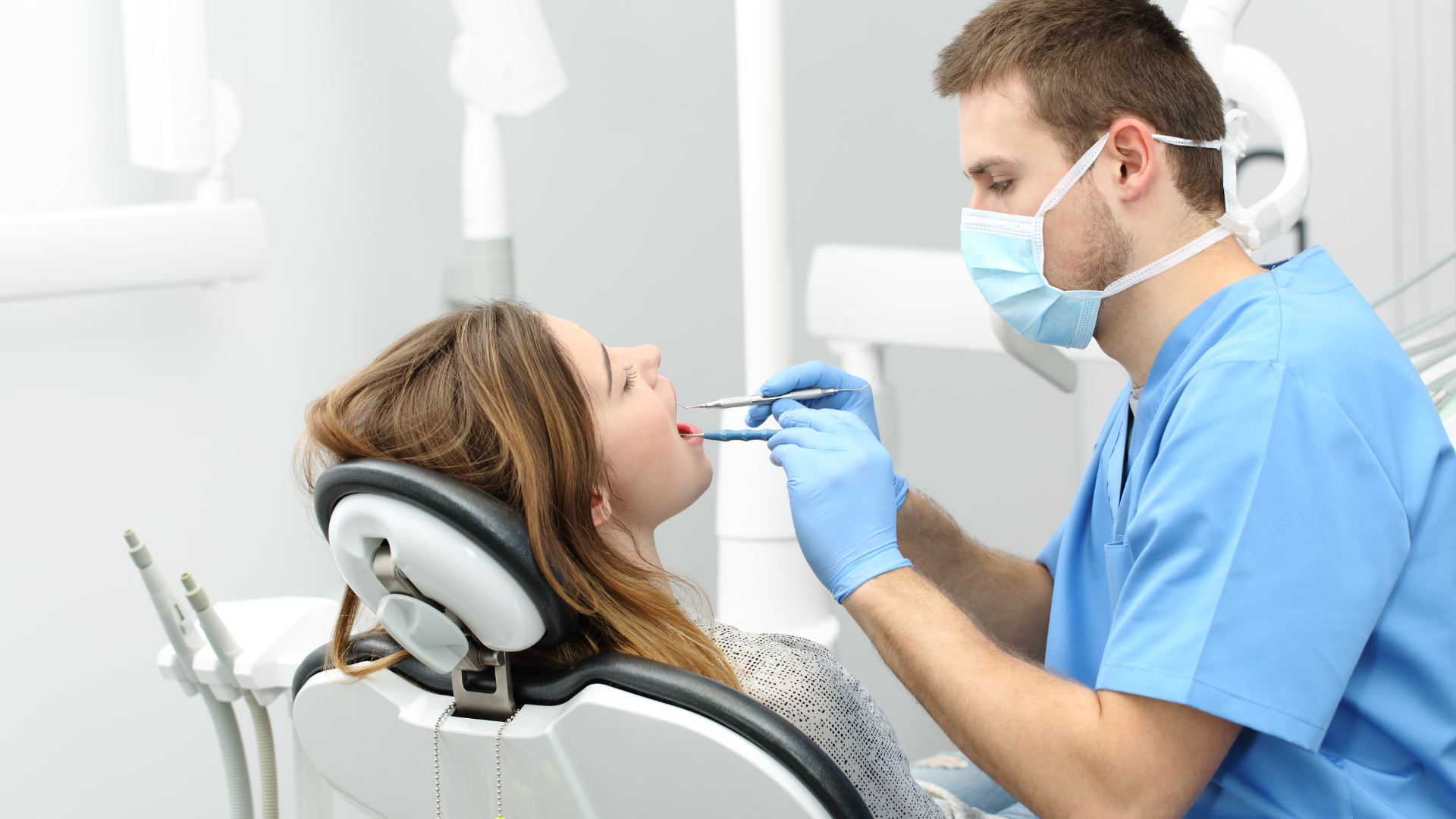 Dentist examining patient's teeth in a dental chair; medical tools visible.