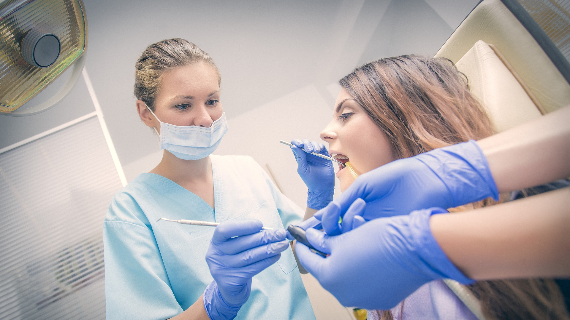 Dentist and assistant treating a patient in a dental clinic, with blue gloves and mask.