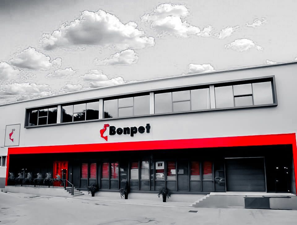 De buitenkant van de Bonpet-fabriek met rode accenten, een reclamebord en een bewolkte lucht.