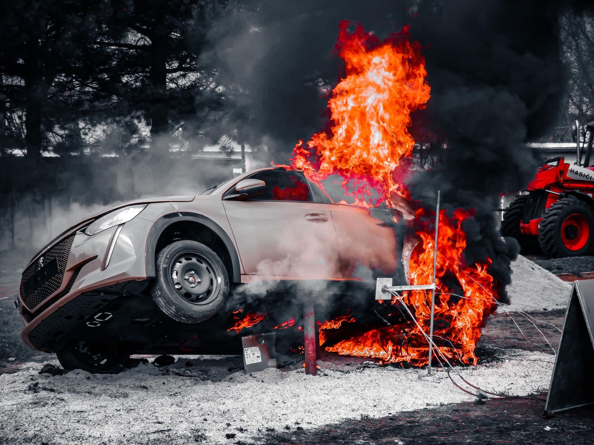Auto staat volledig in brand. Dikke zwarte rookwolken stijgen op. Het vuur woedt hevig vlakbij de voorkant van het voertuig.