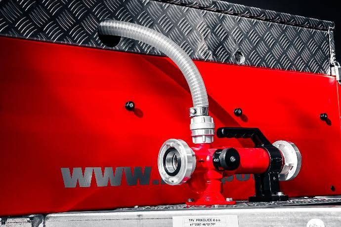 Detail van de waterpomp van een brandweerwagen, rood en zilver, met slang aangesloten op een rode opbergbox.