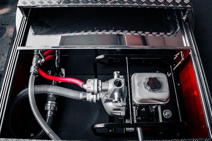 Een zilverkleurige pompmotor in een metalen behuizing. Rode en grijze slangen zijn erop aangesloten.