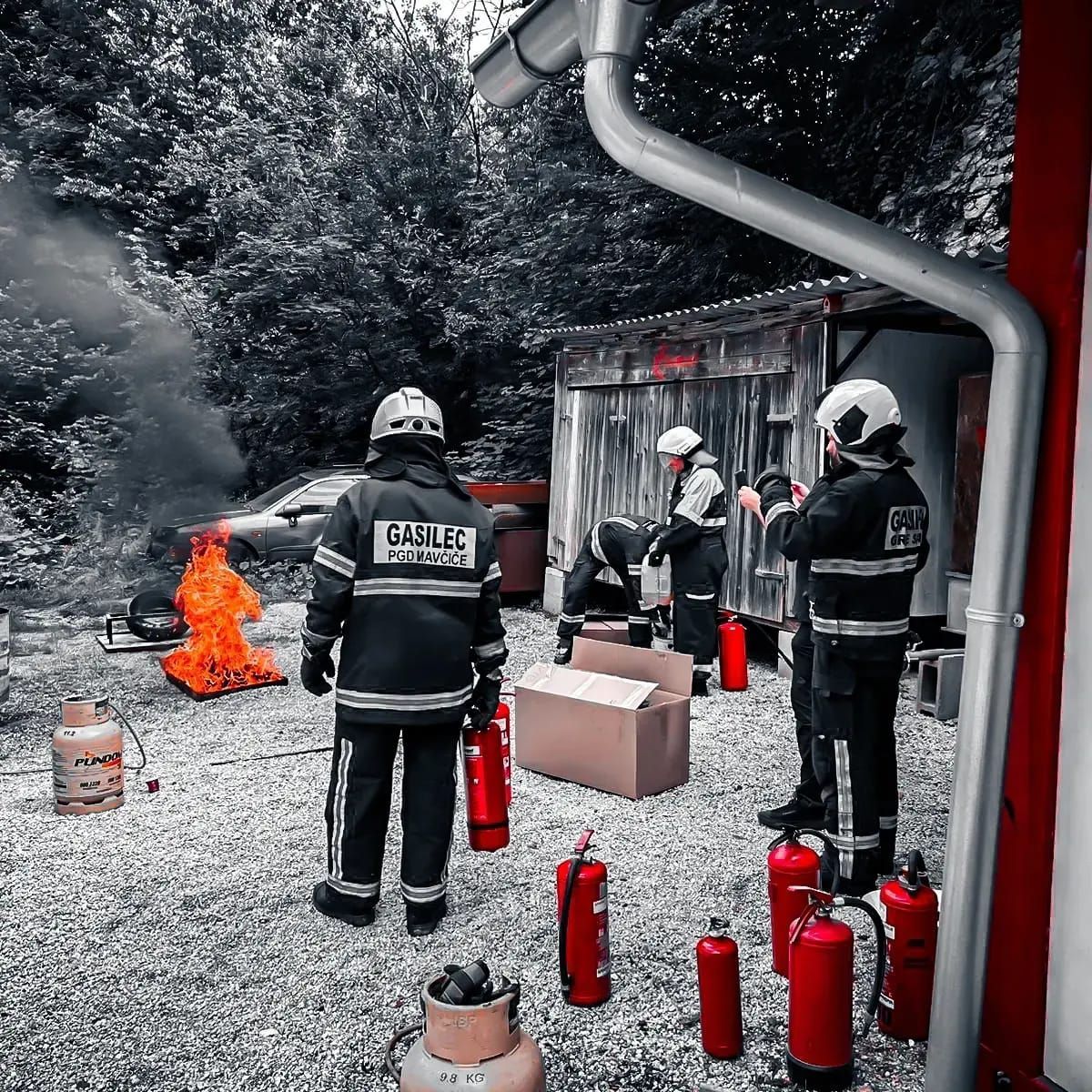 Brandweerlieden oefenen het blussen van een brand buiten een gebouw; een auto staat in brand.