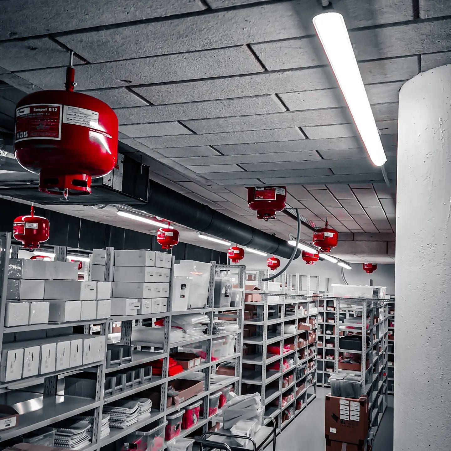 Magazijninterieur met rijen schappen vol dozen en een rood brandblussysteem.