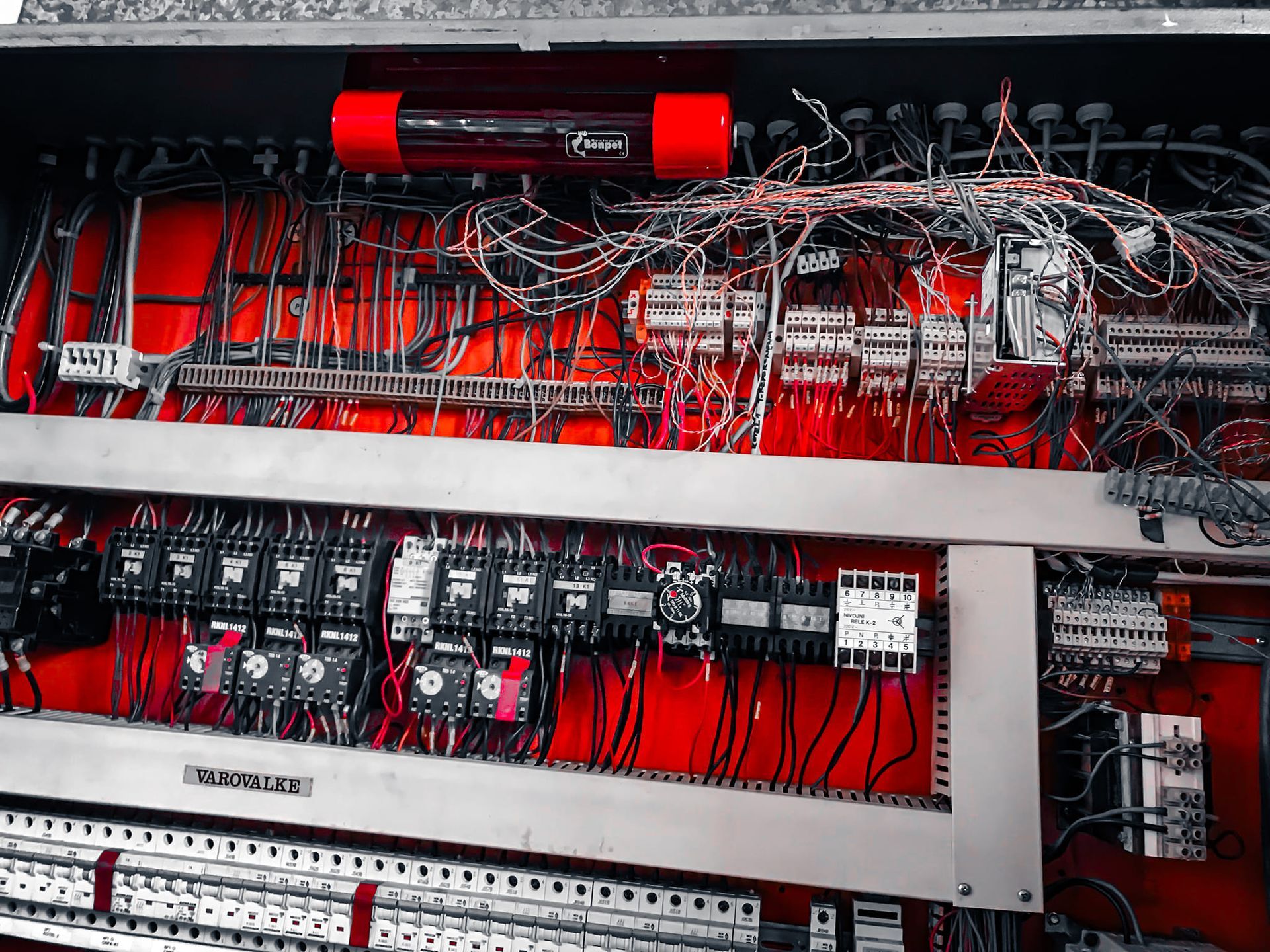 Rood elektrisch schakelpaneel met diverse draden, relais en componenten.