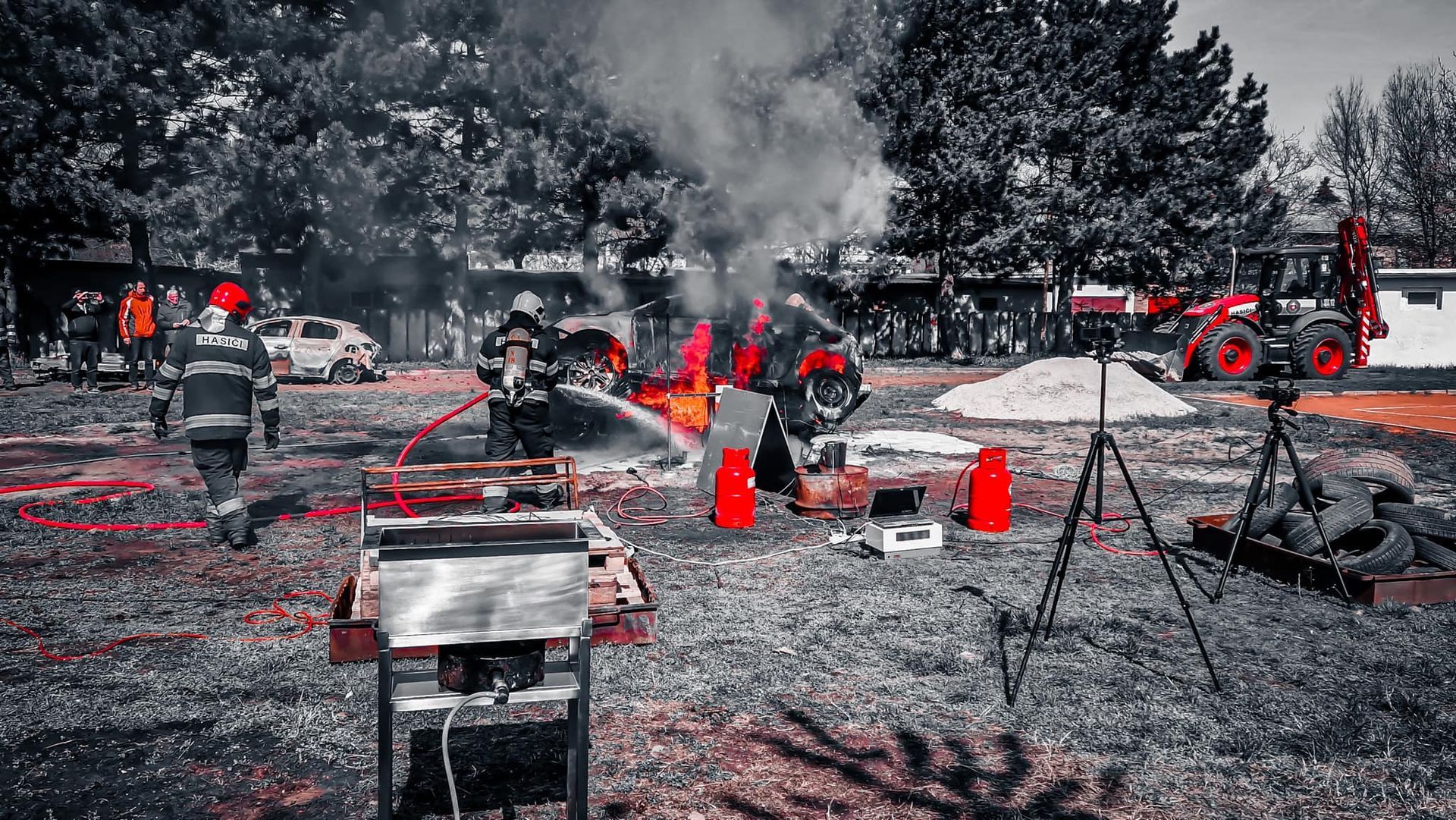 Brandweerlieden bestrijden een openluchtbrand met slangen; tractor en veiligheidskegels zichtbaar.