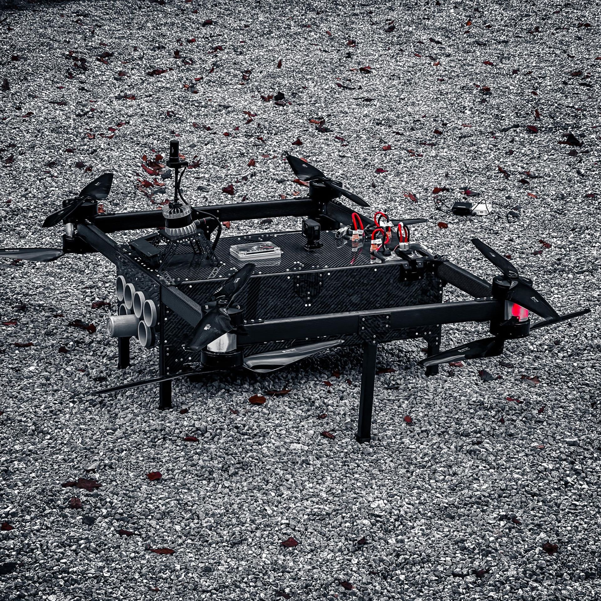 Zwarte drone met rotors, neergestreken op een met kiezels bezaaide ondergrond.