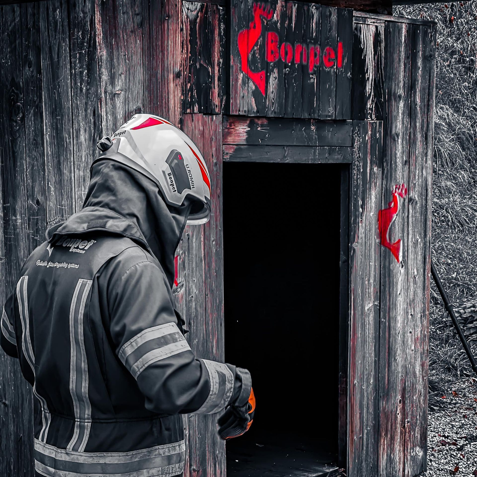 Brandweerman in uniform, met helm, voor een donkere deuropening, houten constructie met 