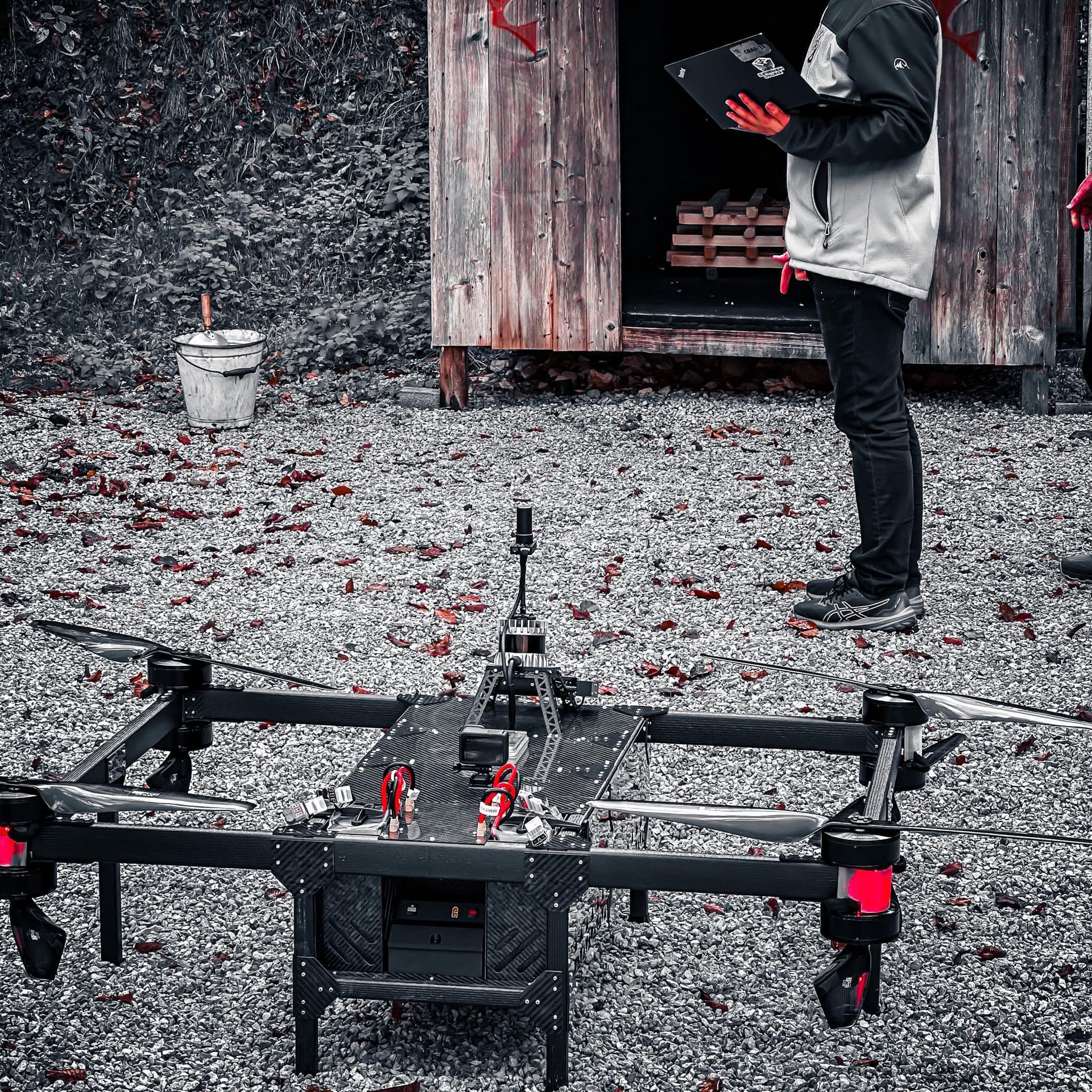 Een drone op de grond met een persoon die bij een houten gebouw staat en een klembord vasthoudt.