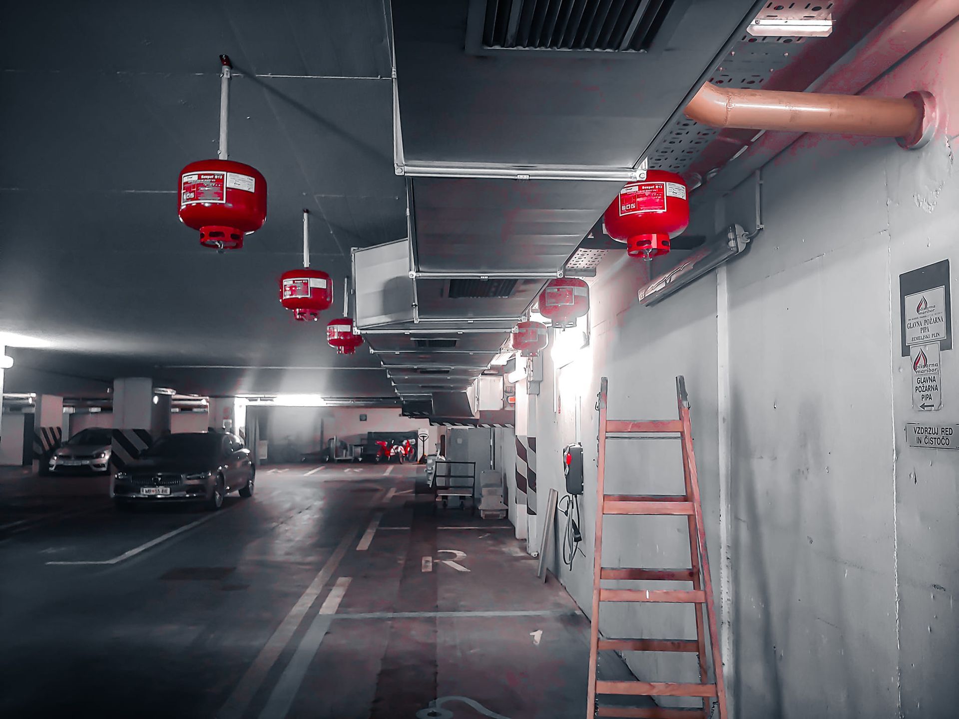 Ondergrondse parkeergarage met auto’s en rode plafond gemonteerde brandblussystemen.