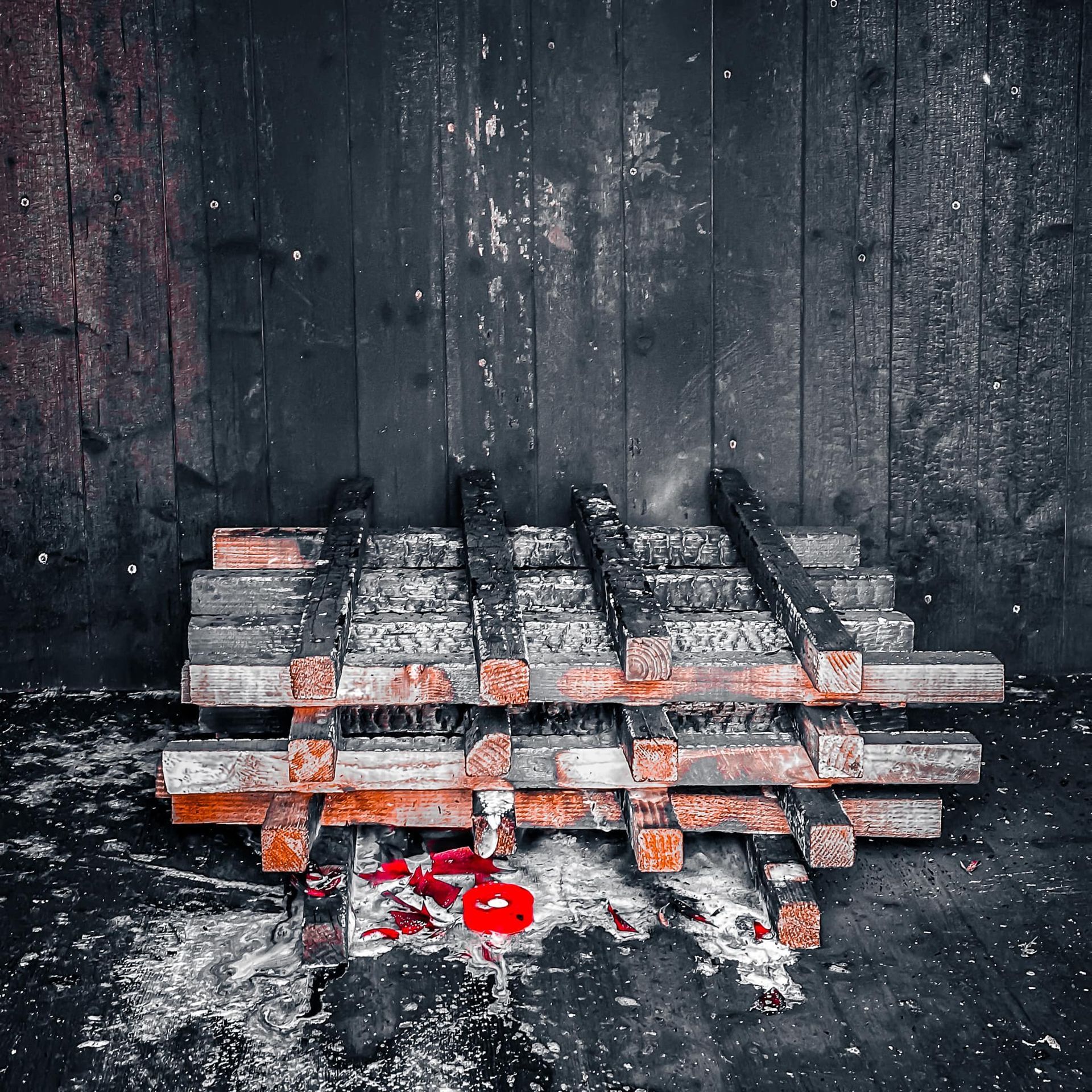 Een stapel verweerd, rood omrand hout tegen een donkere, afbladderende muur en vloer, waar nog wat rode verf zichtbaar is.