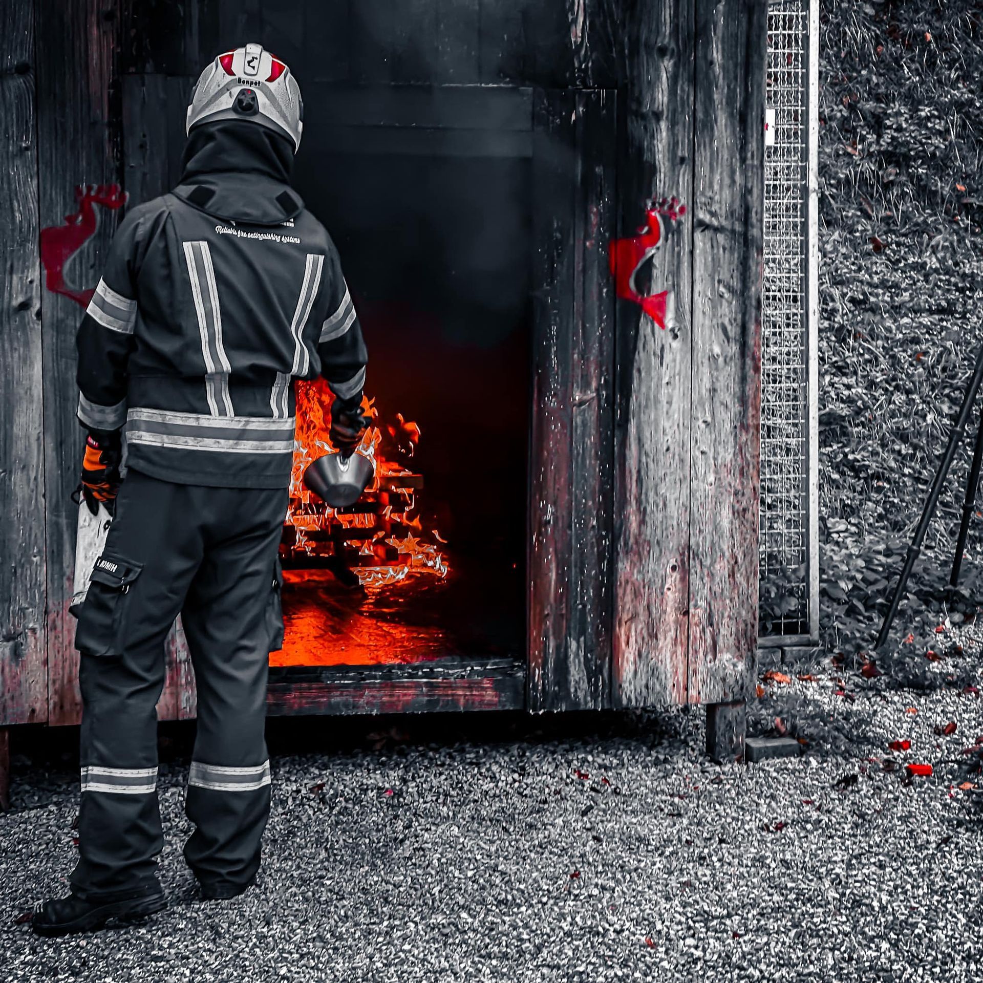 Brandweerman in beschermende kleding voor een brandende houten constructie.