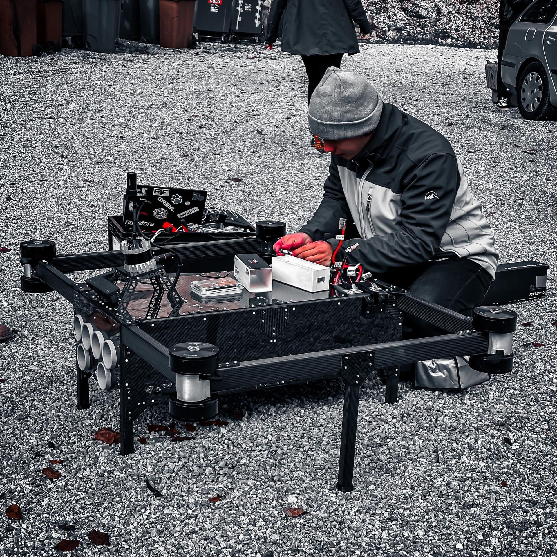 Man werkt buiten aan een dronetafel met gereedschap en onderdelen. Grijstinten afbeelding.