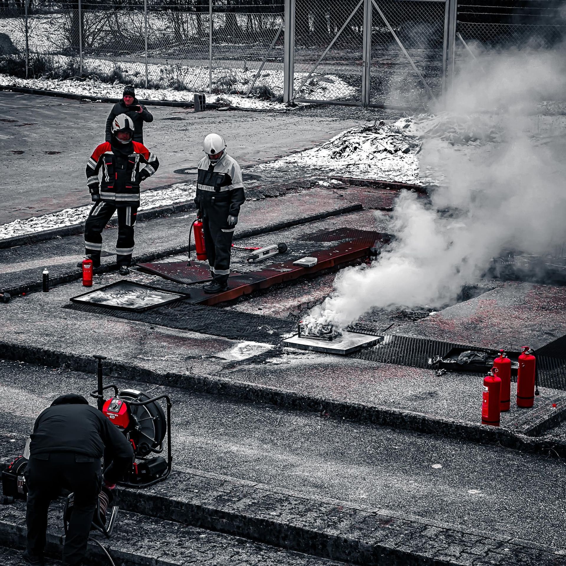 Brandweerlieden op een oefenterrein met rook en een kleine brand.