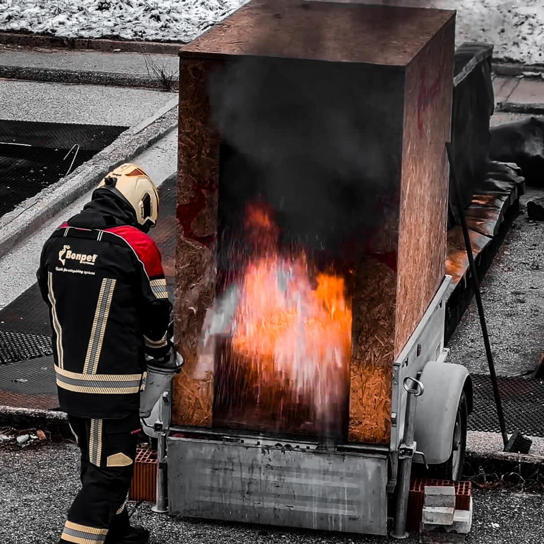 Brandweerman bestrijdt brand bij een rechthoekig gebouw, met zichtbare oranje vlammen.