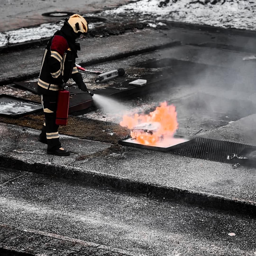Een brandweerman blust een brand op een dak, waarbij vlammen en rook zichtbaar zijn.