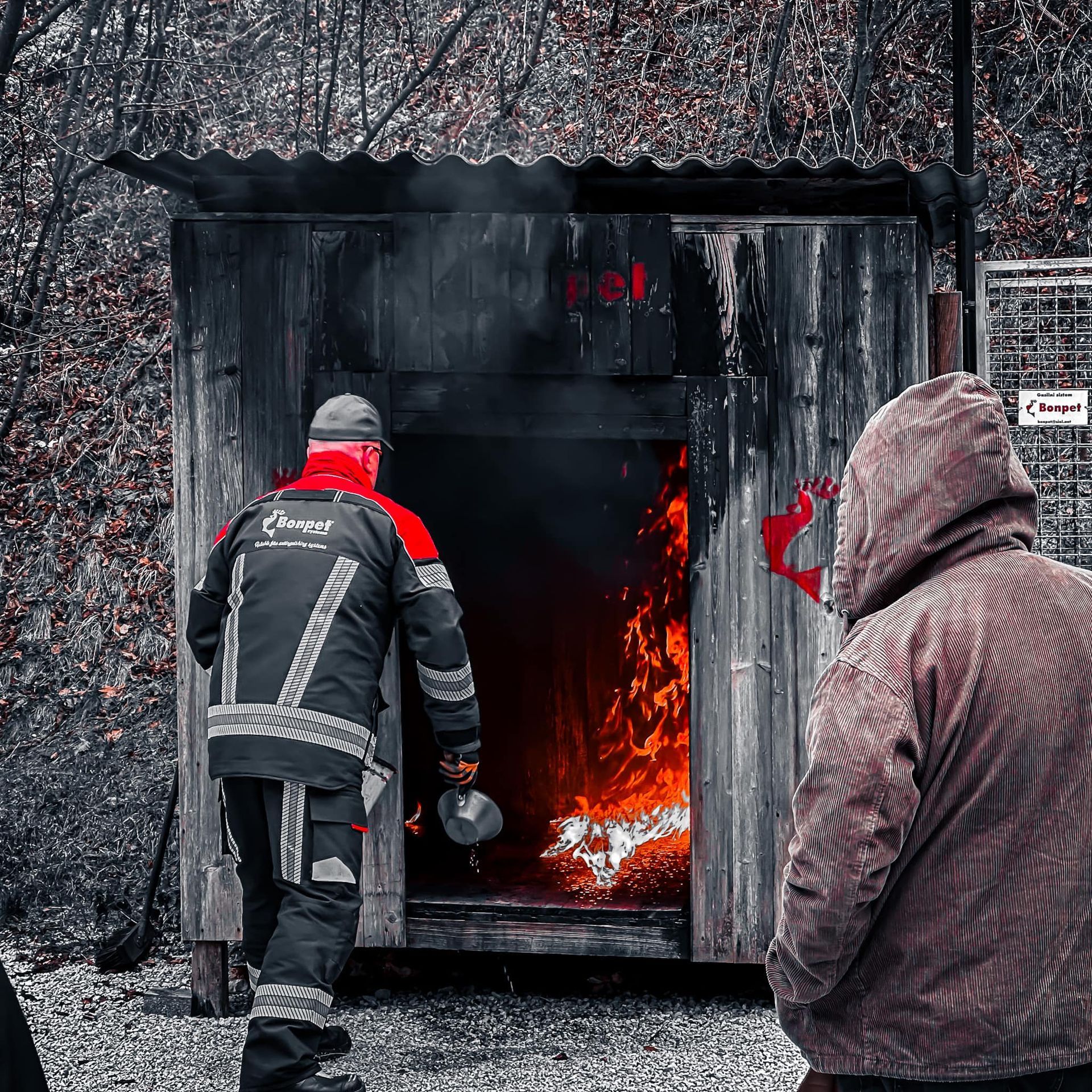 Een brandweerman betreedt een brandend gebouw; hevige vlammen, een andere persoon kijkt toe.